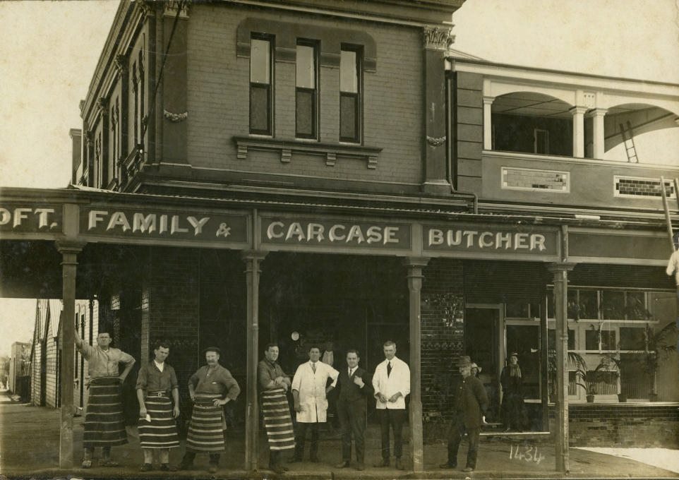 Scan of a photgraph from 1900 of people standing outside a butchers shop. 