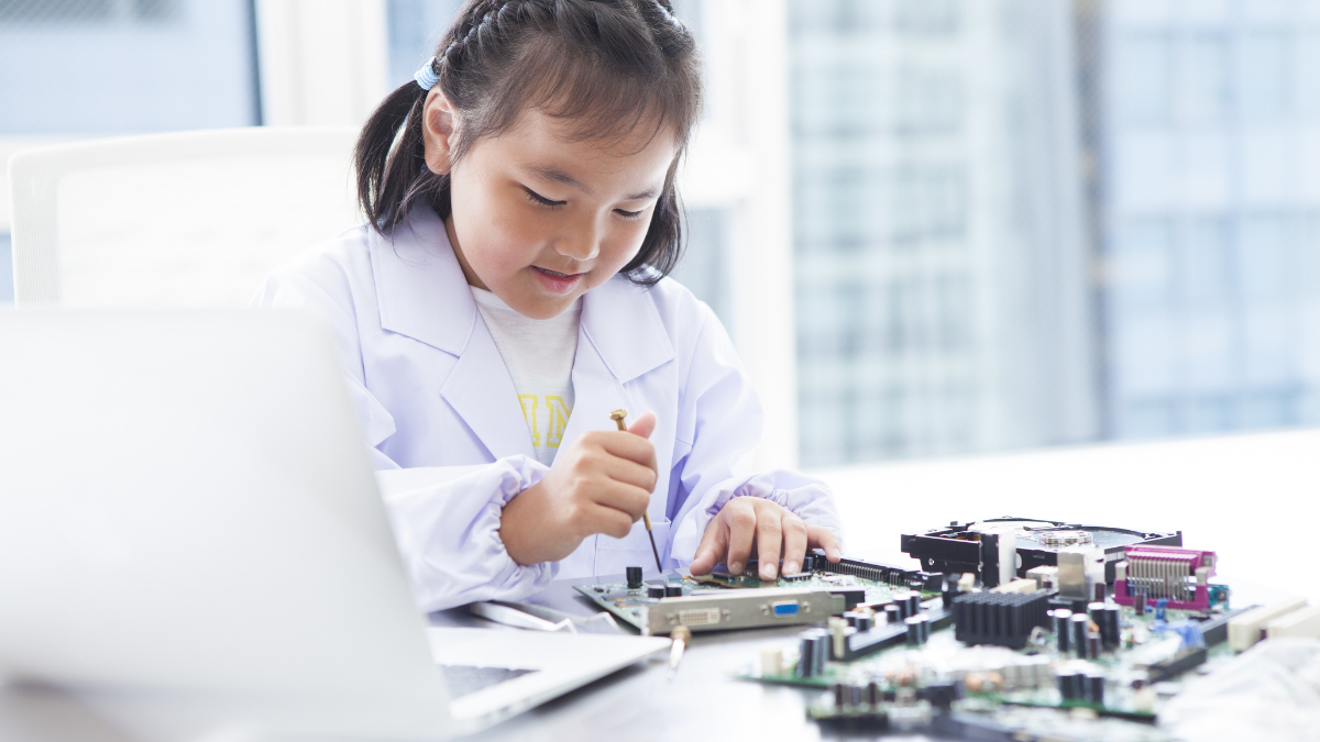Young girl in lab coat tinkering with electronics